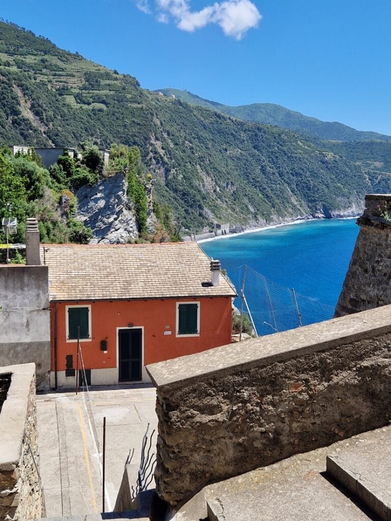 Corniglia - Kohti avaraa maailmaaMaisema oli häkellyttävän kaunis – mutta aivan sen keskellä lojui rytökasojen ja muovin peittämä piha. Pesuallas seinää vasten, tiskiainepullo valmiina, ja vieressä kasa lautoja, metalliputkia ja muovilaatikoita. Paras mahdollinen sijainti, kaunein mahdollinen näkymä – ja silti kaikki hylätty, kuin elämä olisi pysähtynyt. Cornigliassa on jotakin syvästi ristiriitaista. Täällä ruostunut kaide ja villiintynyt kasvi voivat kasvaa aivan unenomaisen sinisen meren yllä, ja joku kuitenkin jättää kaiken hoitamatta. Ehkä se juuri tekee tästä paikasta niin todellisen.